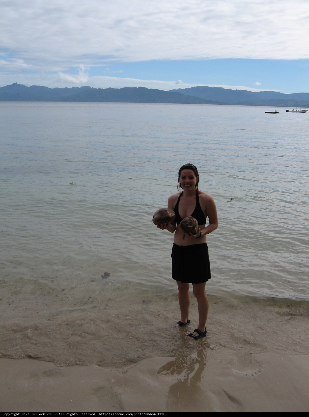 Smiling Woman Holds Coconuts on Fijian Beach