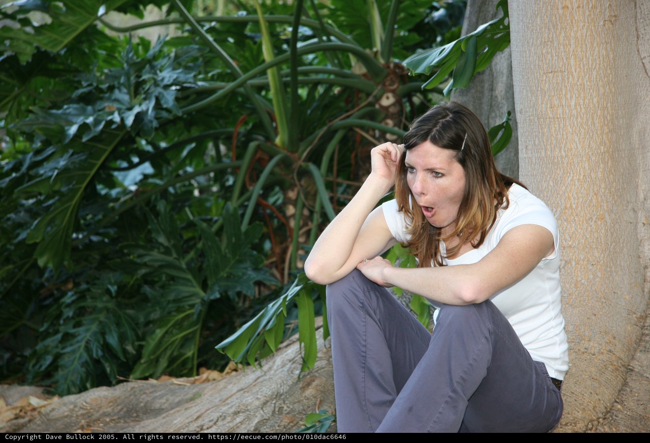 Surprised Woman Crouching by Tropical Garden Wall