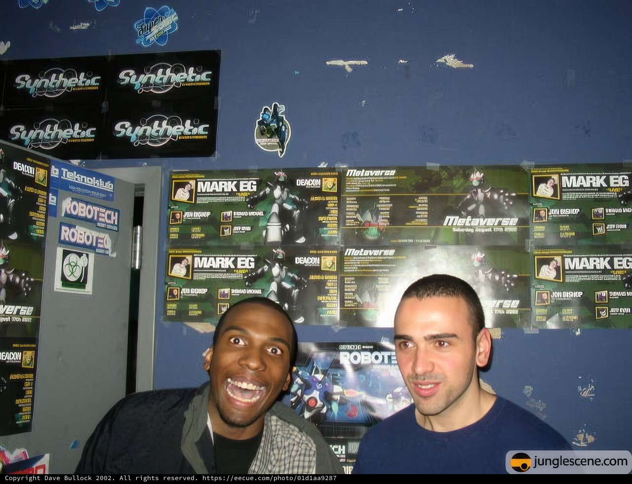 Two Men Posed in Front of Computer Hardware Posters