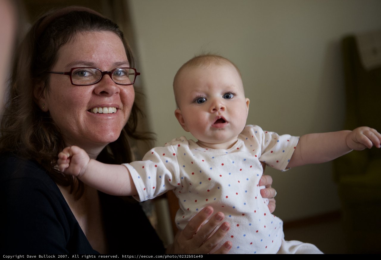 Joyful Mother Holds Wide-Eyed Baby Indoors