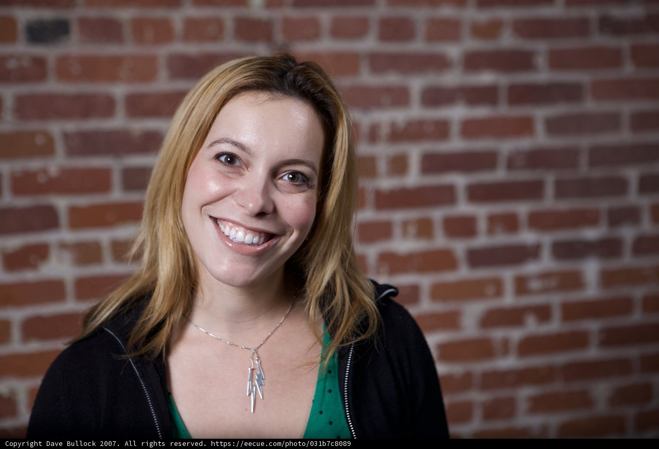 Smiling Woman in Green Shirt against Brick Wall