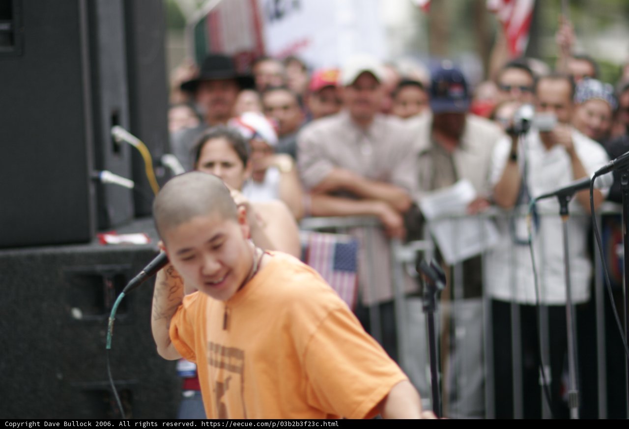 Man in Orange Shirt Addresses Crowd with Microphone