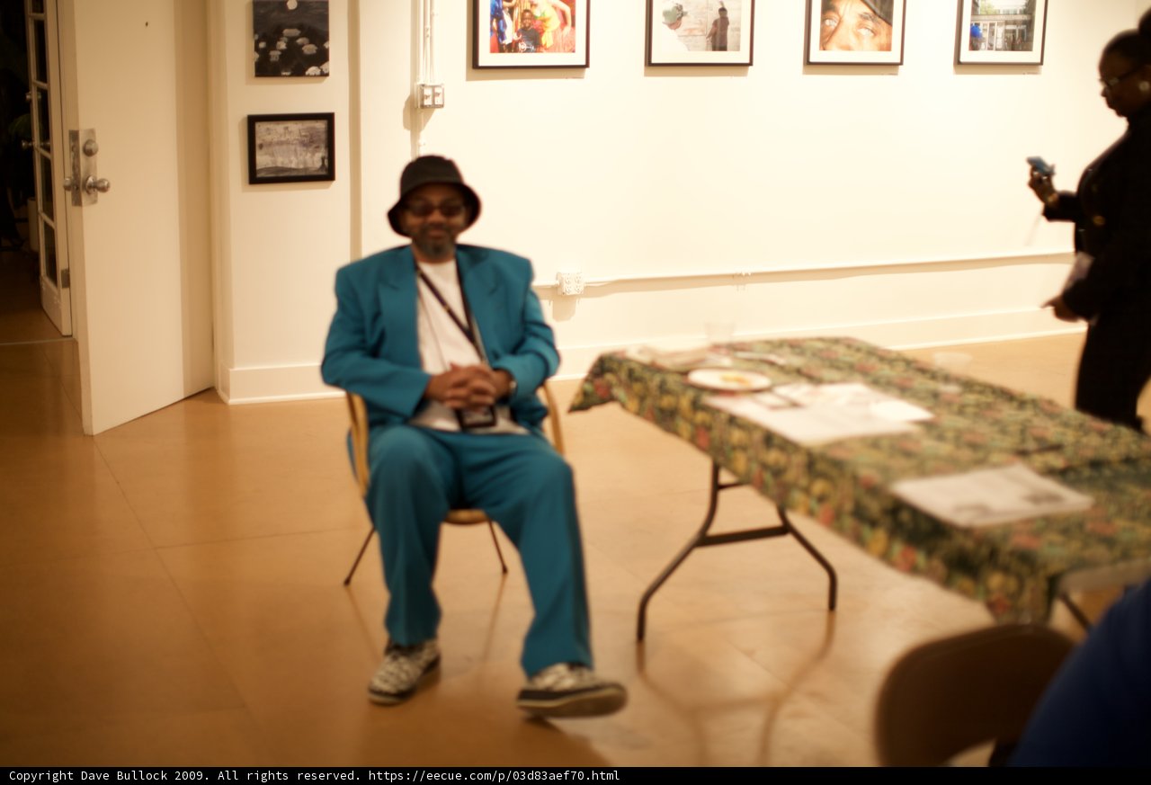 Blue Suited Man Sitting on Hardwood Chair in Art Gallery