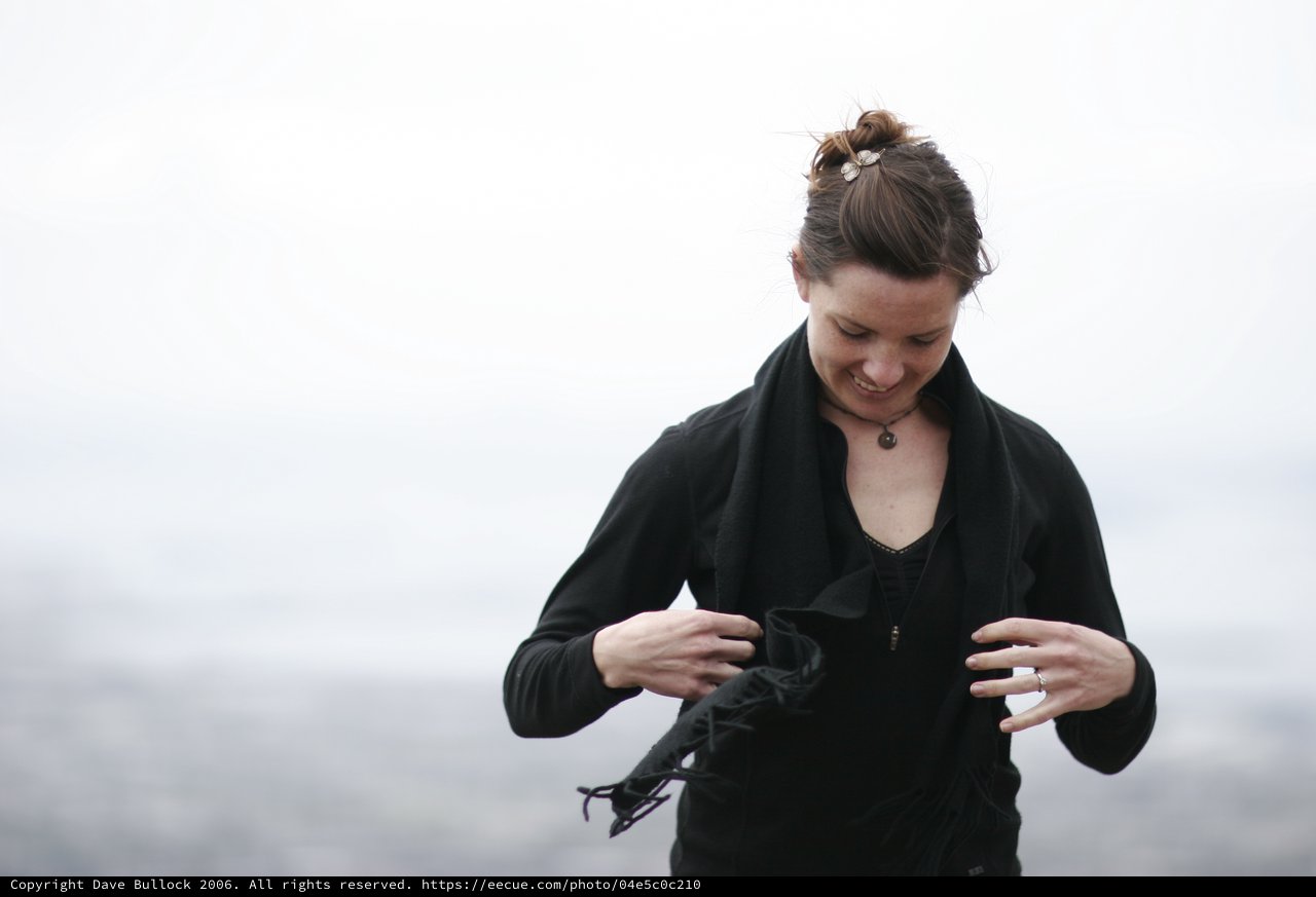 Woman in Black Adjusting Scarf in Coastal Wind
