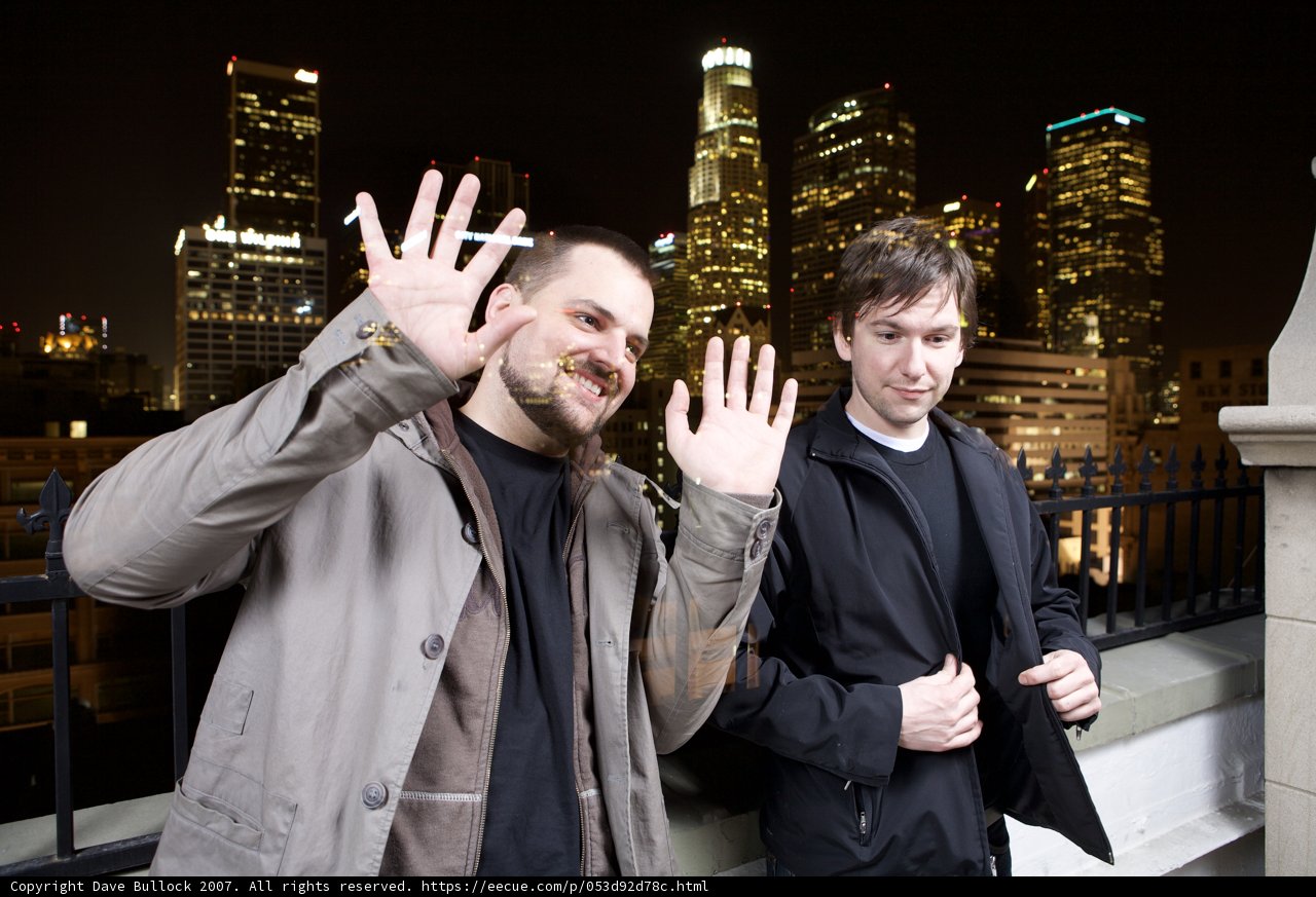 Two Men in Overcoats Pose in Front of Urban Metropolis