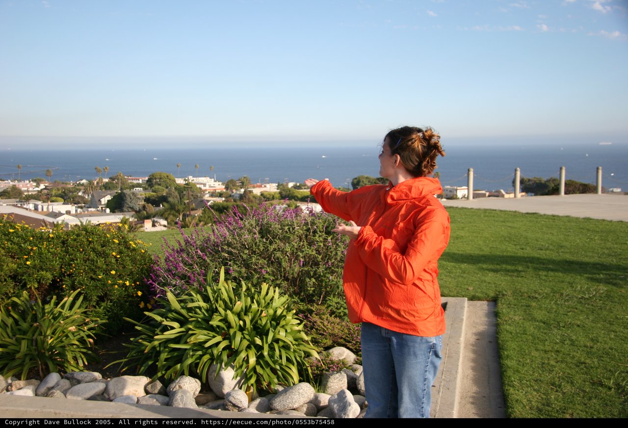 Woman Gesturing Toward Ocean View from Hilltop Garden