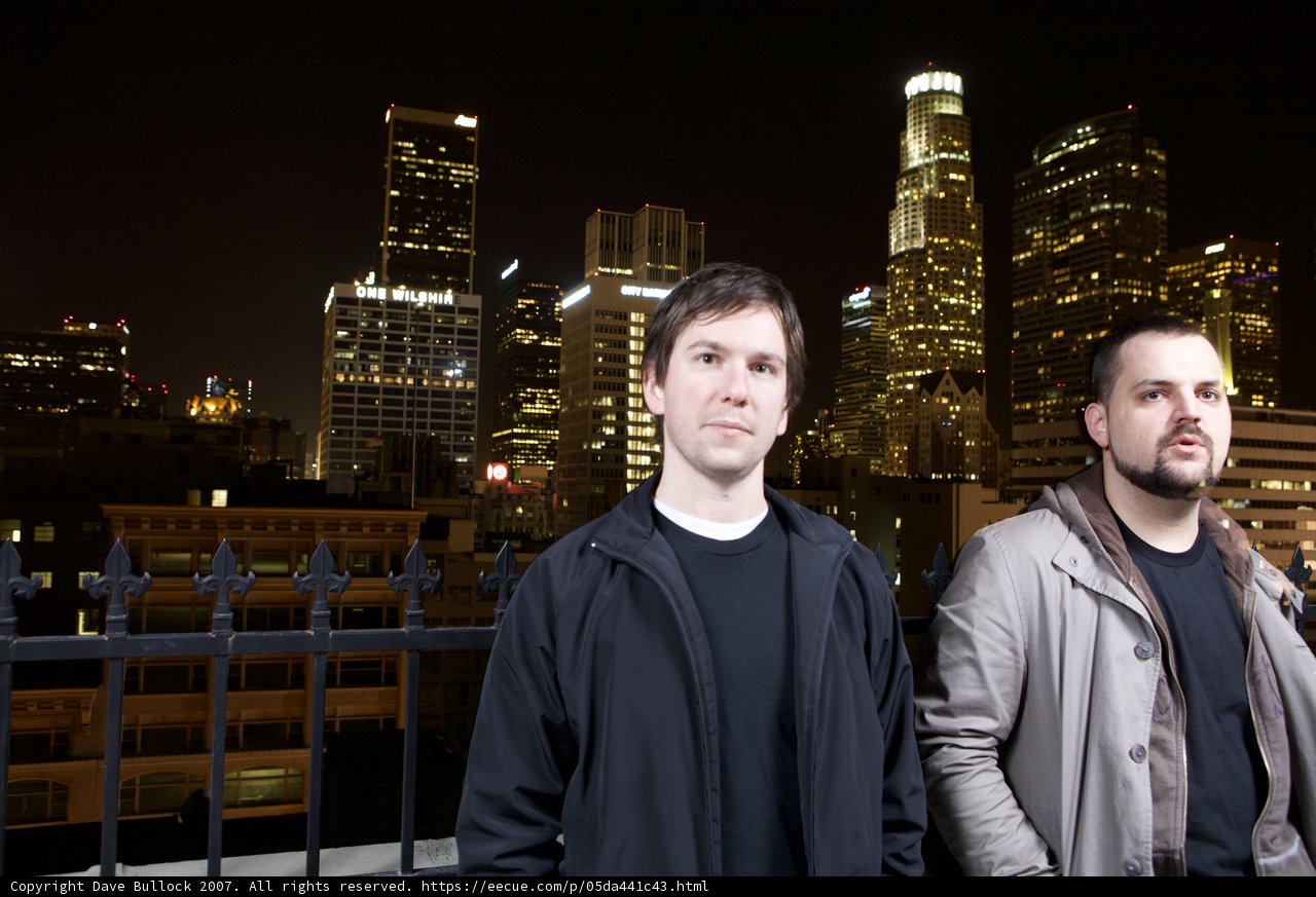 Two Men in Overcoats Stand before a Metropolitan Skyline