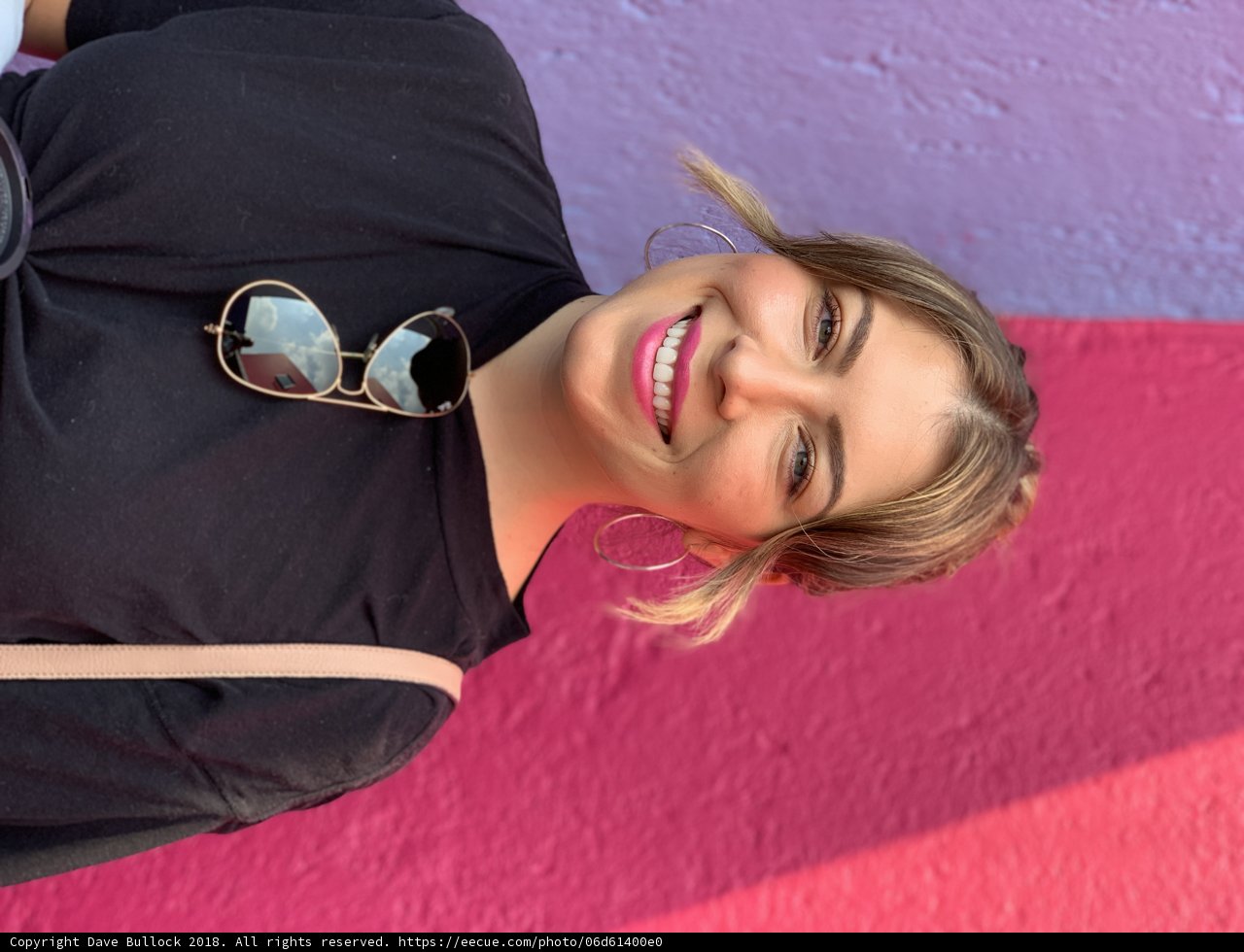 Smiling Woman in Sunglasses Poses in Front of Colorful Wall