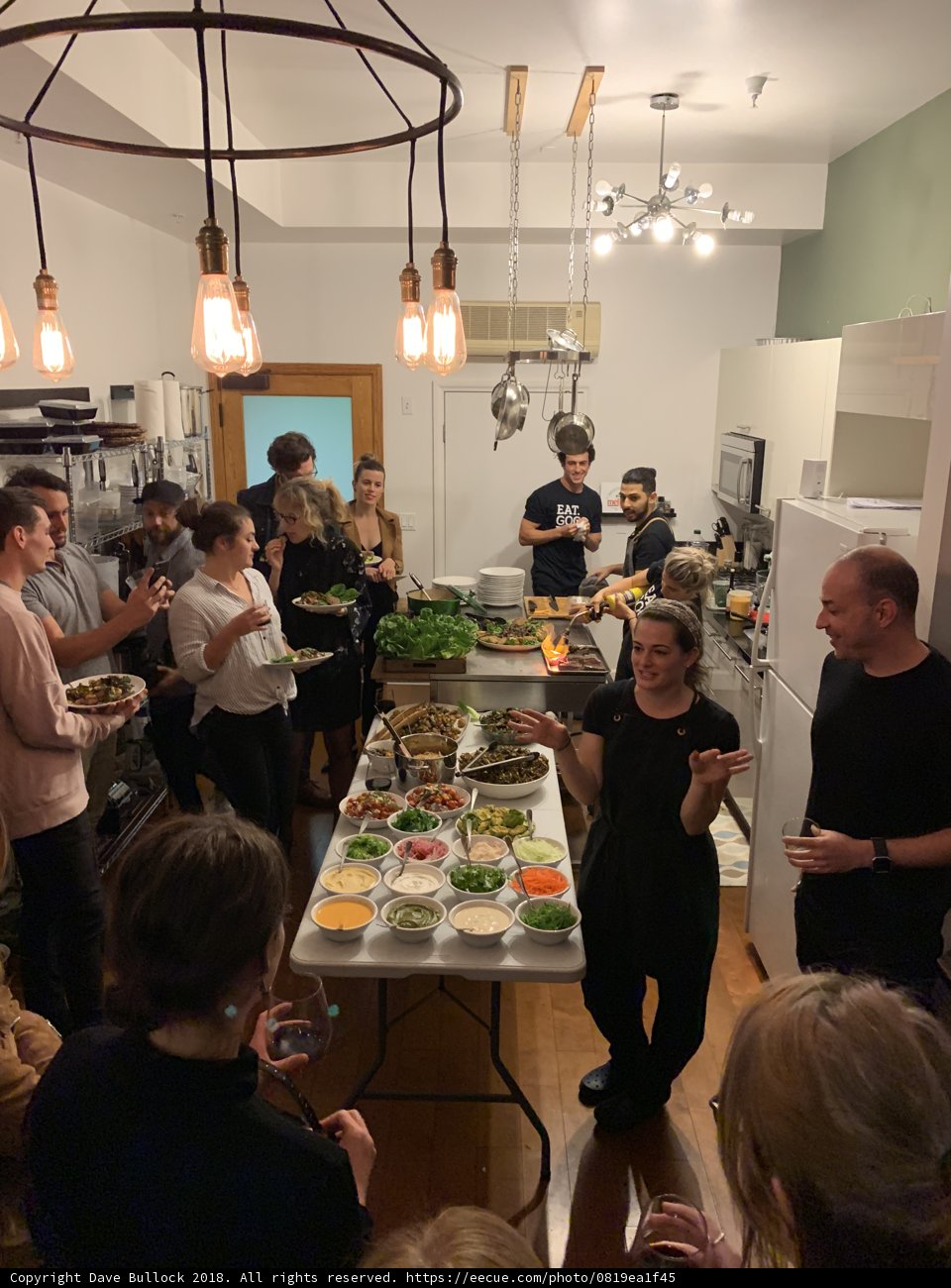 Meal time with friends Caption: A group of 15 people enjoy a buffet meal together in a restaurant kitchen in Los Angeles, California. The chandelier and plants in the background add to the stylish and relaxed atmosphere.