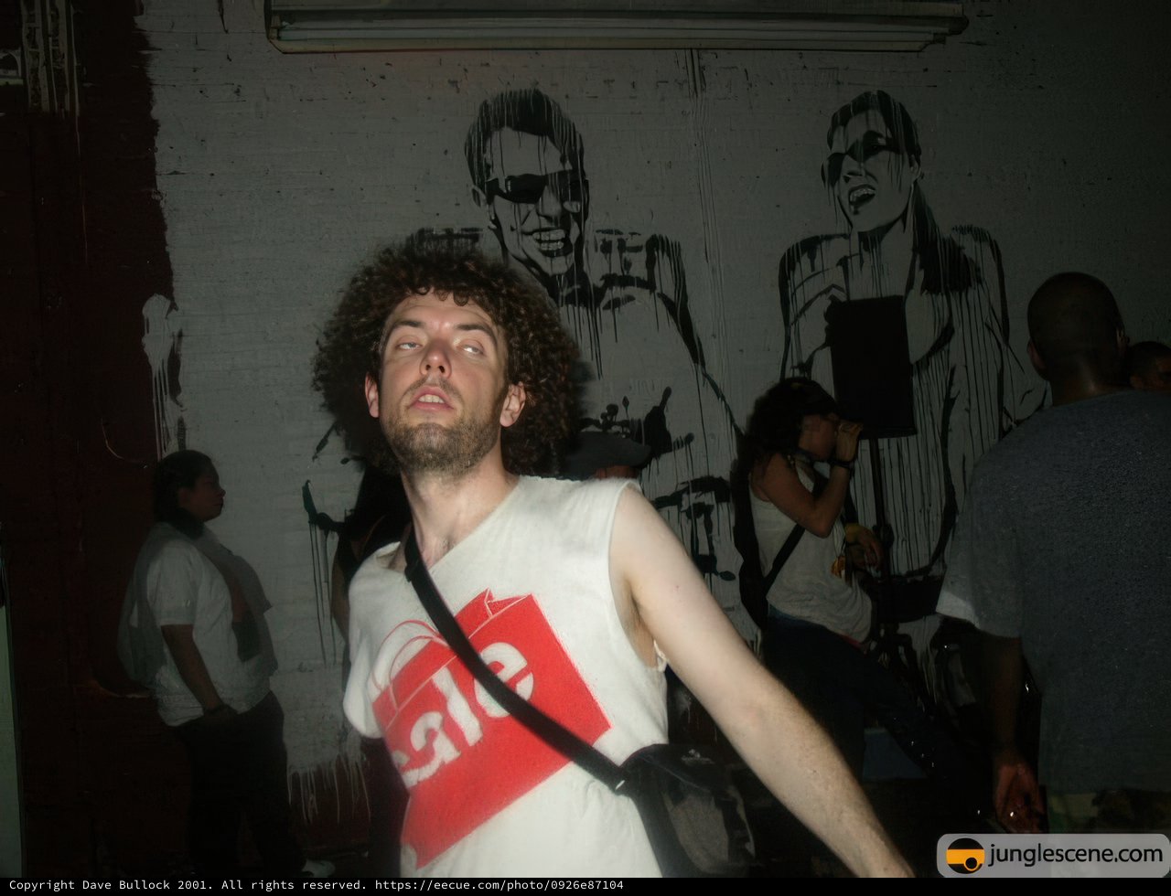 Curly-haired man posing in front of graffiti wall