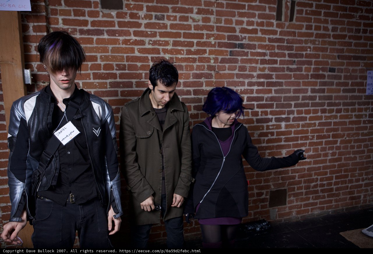 Three Adults in Jackets Standing by Brick Wall