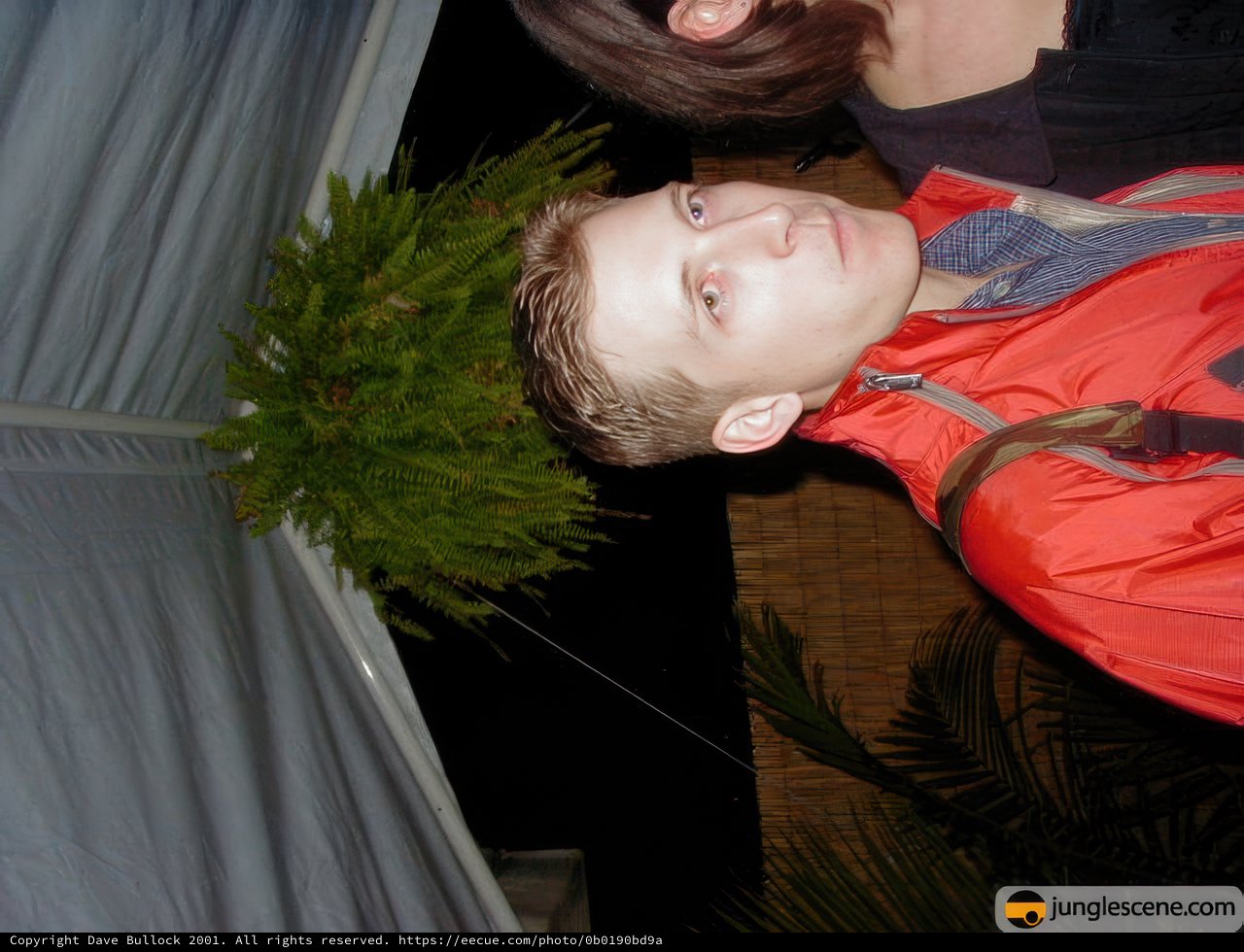 A Man in a Red Jacket Poses with a Potted Plant and Tree