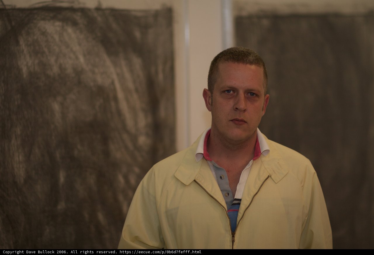 Man in Yellow Coat Poses in front of Black and White Painting