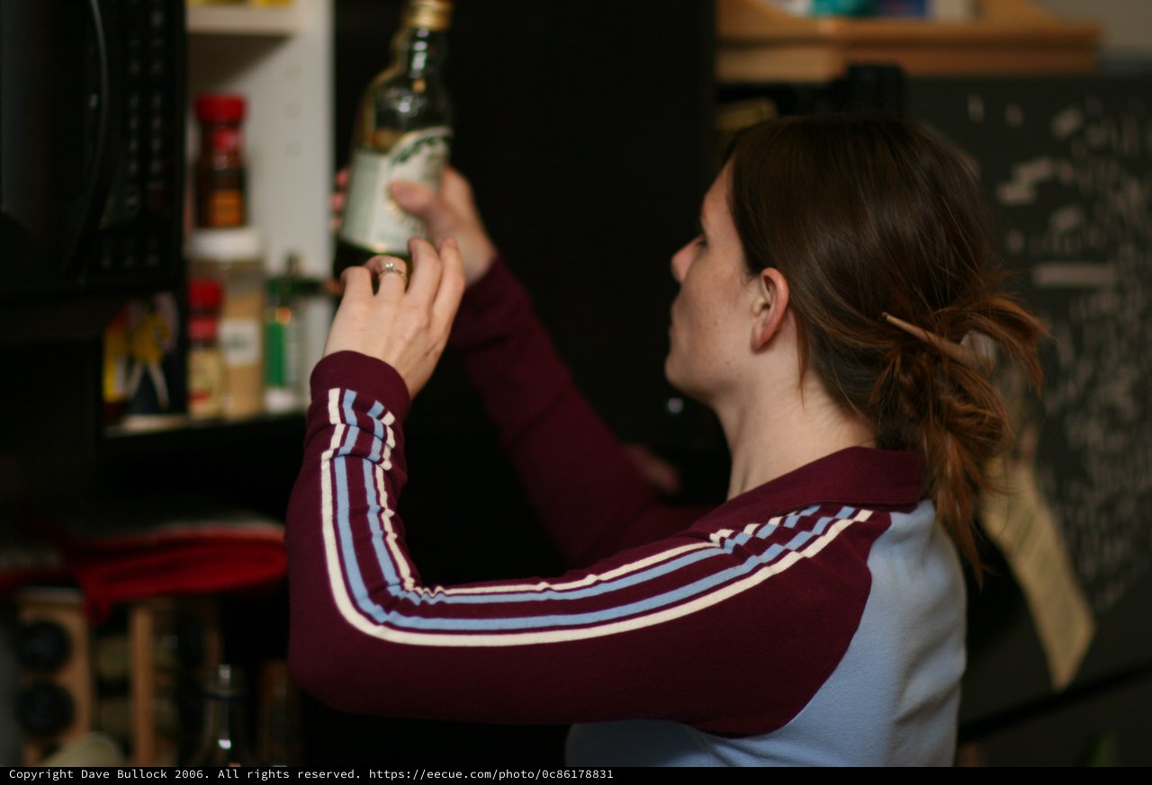 Woman Examining Bottle in Dimly Lit Kitchen