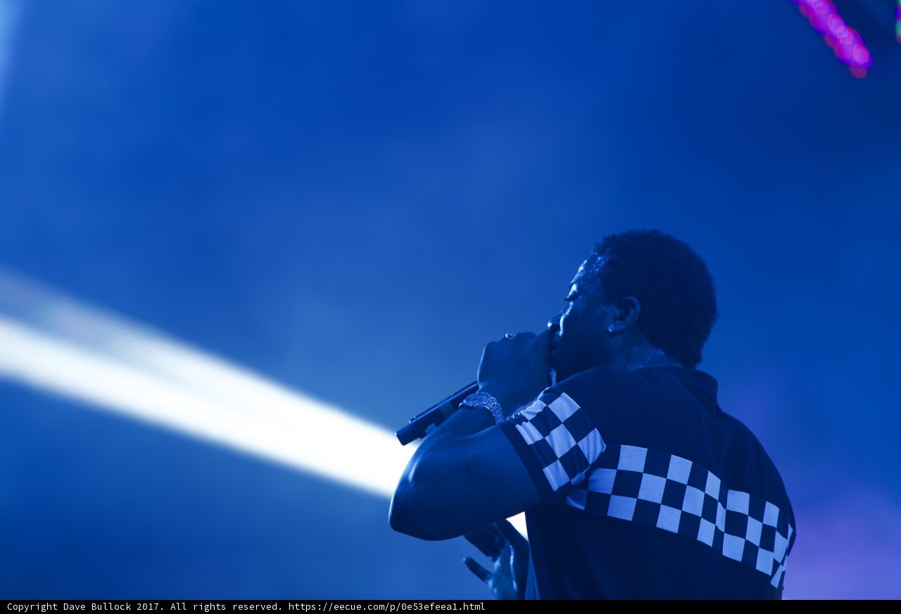Spotlight on the Entertainer Caption: A man in a checkered shirt mesmerizes the crowd with his solo performance at Coachella 2017, under the vibrant glare of the spotlight.