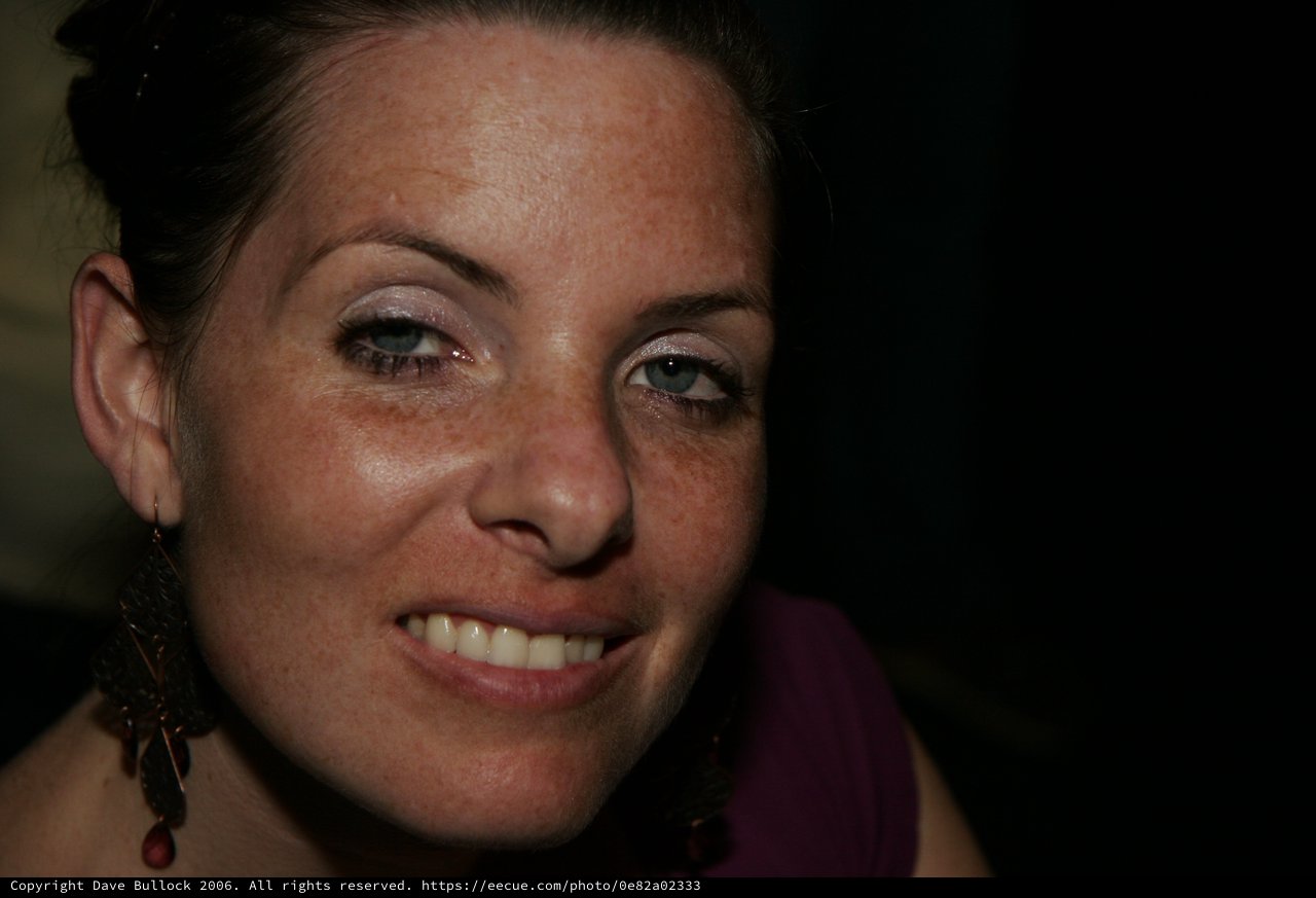 Freckled Woman with Blue Eyes Smiling in Dark Setting