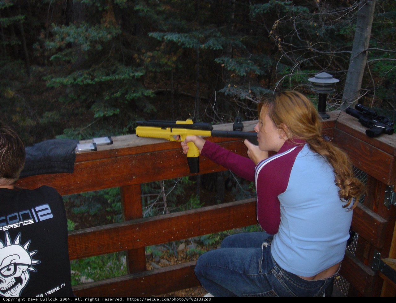 Young Woman Aiming Yellow Air Pistol on Wooden Deck