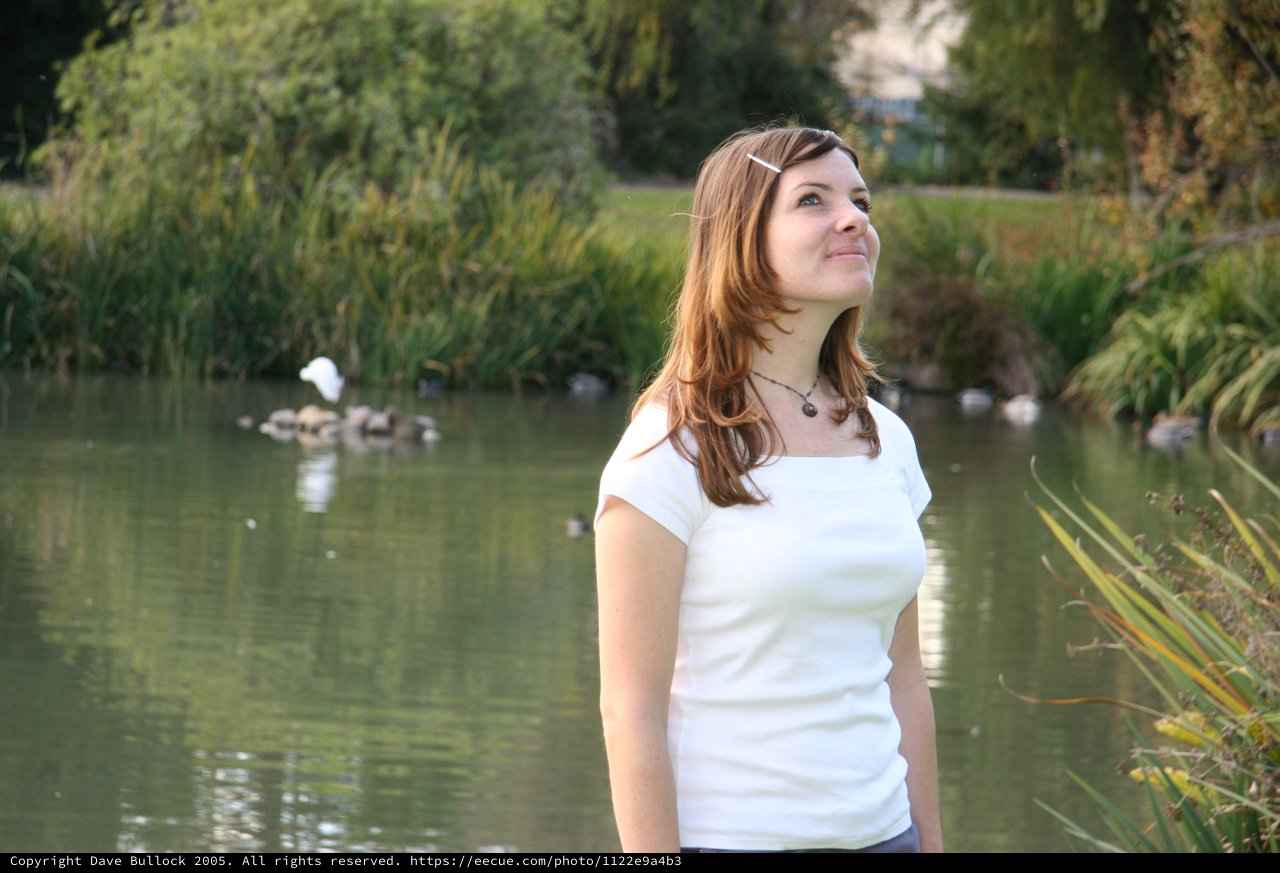 Young Woman Gazing Upward by a Peaceful Park Pond