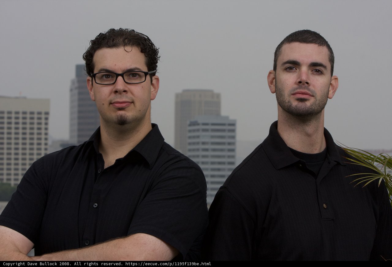 Two Happy Men in Black Shirts Pose Outside Skyscraper