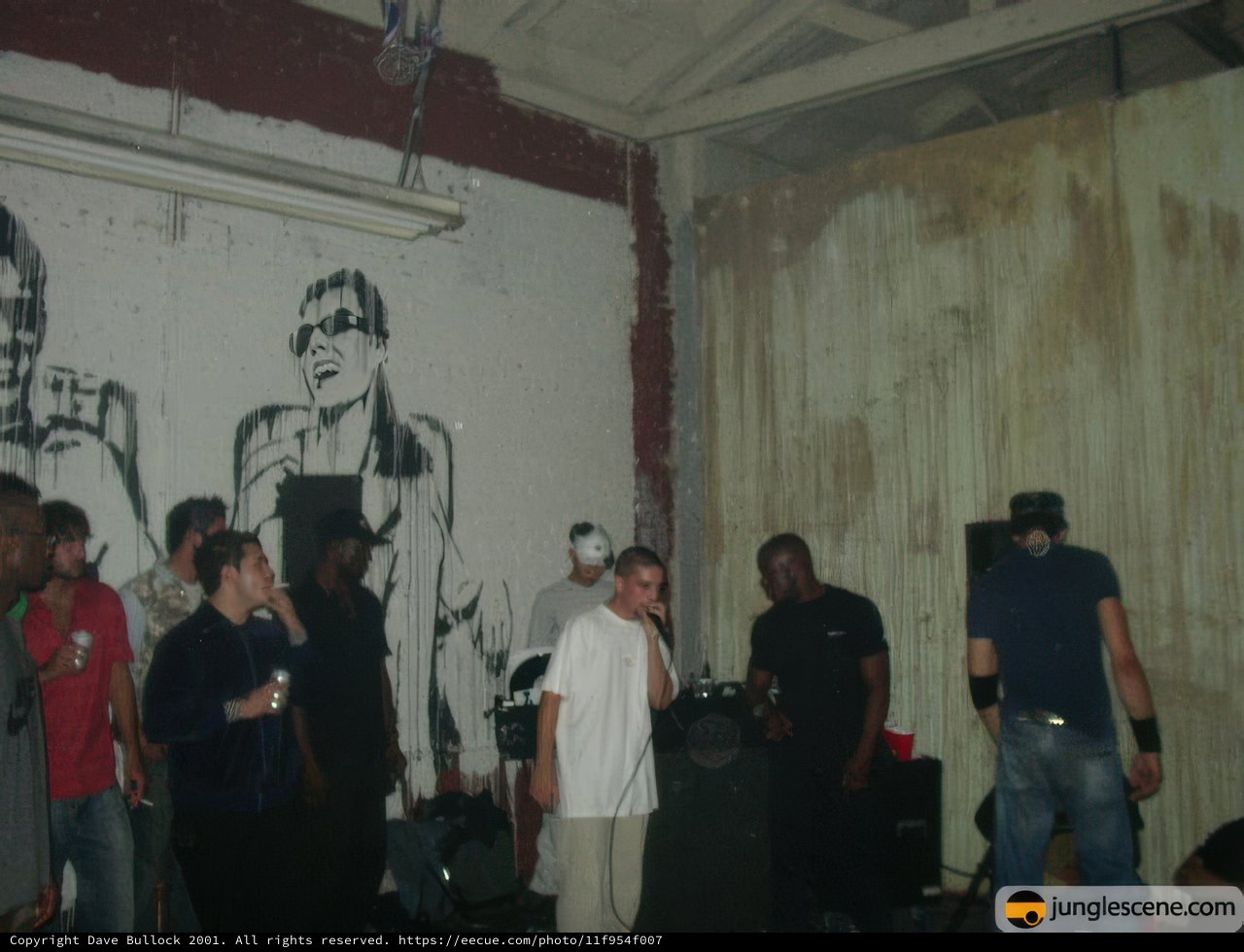 Graffiti Gathering Caption: A group of 12 people, including 6 men and 6 adults, stand in front of a wall covered in vibrant graffiti. The urban backdrop is the perfect setting for their casual clothing and accessories, including jeans, T-shirts, hats, bracelets, and cups.