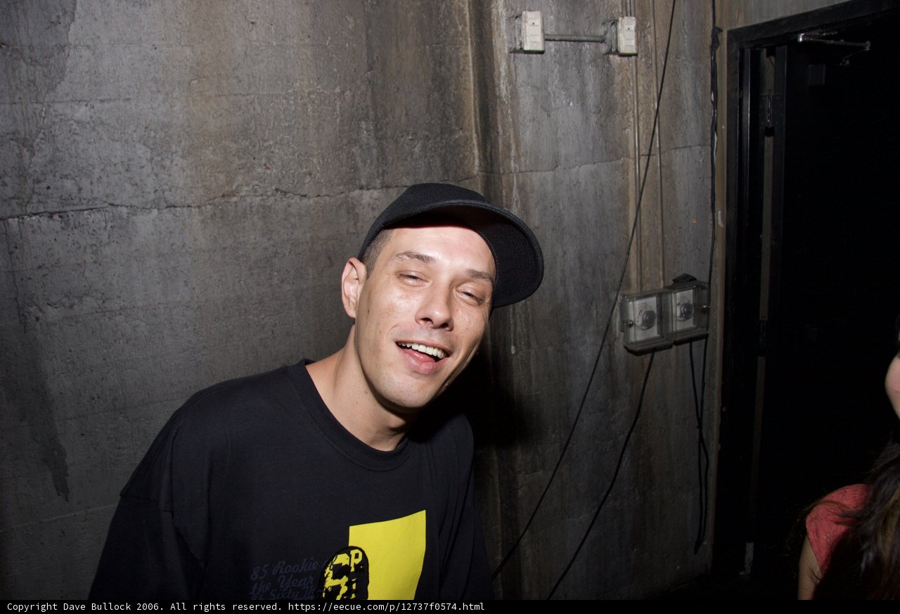 DJ S sporting a black hat and shirt with a smile
