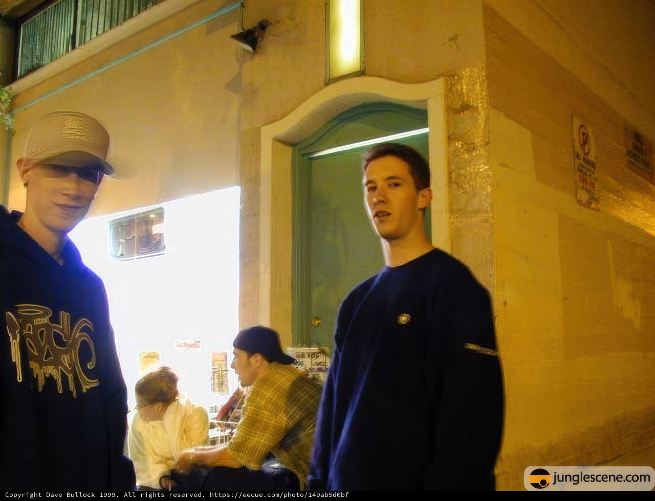 Two Men in Hats Pose in Front of Building at Night