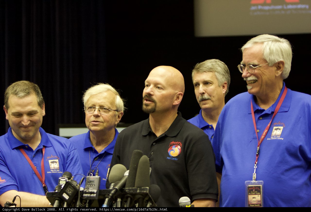 Press Conference with Five Men Standing Behind Microphones