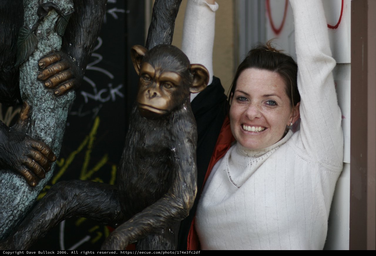 Woman Poses Playfully Beside Bronze Chimp Sculpture