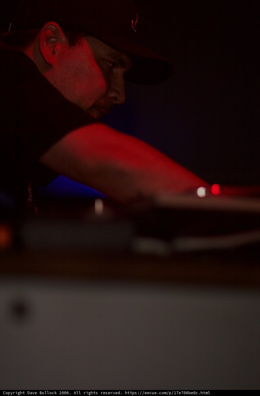 The DJ in the Black Hat Caption: This man, wearing a black shirt and hat, expertly spins tracks to keep the crowd moving at the nightclub.