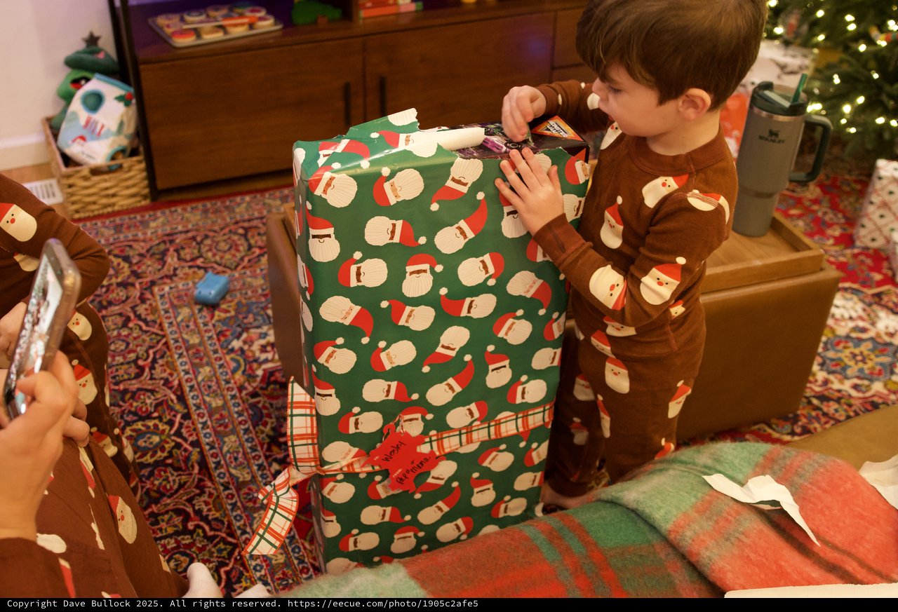 Christmas Morning: Child Unwrapping Santa-Themed Present