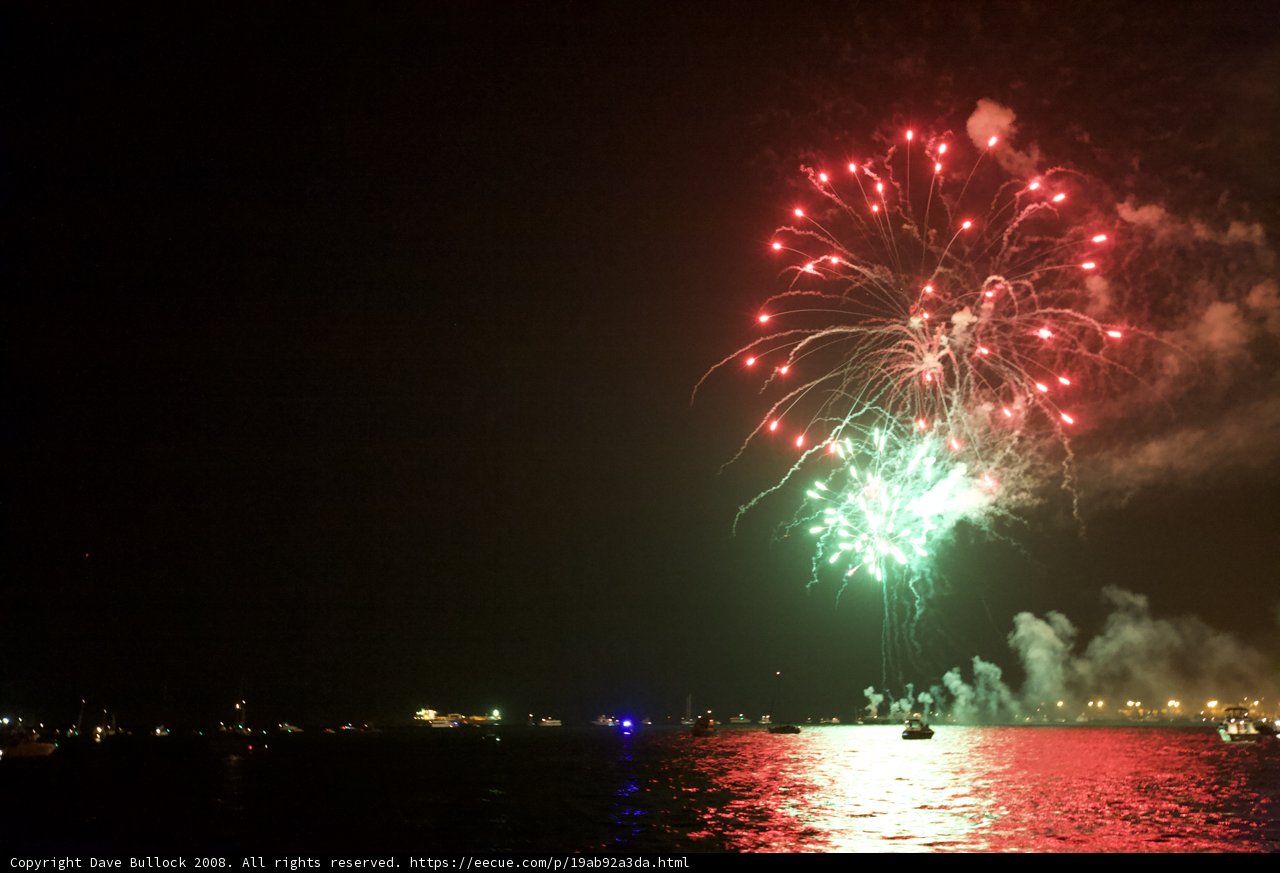 Fourth of July Spectacular on the Water Caption: A dazzling display of pyrotechnics lights up the night sky over six boats and two cars on the water, creating an unforgettable Fourth of July celebration.