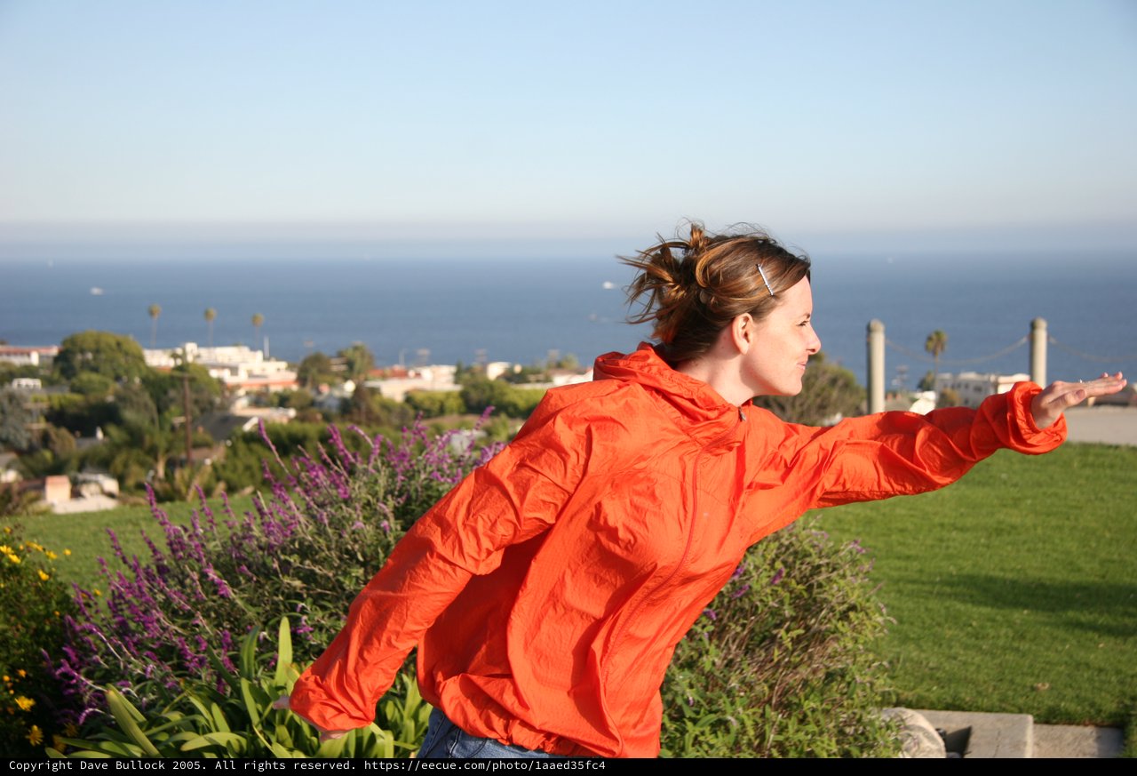 Woman in Orange Jacket Embracing Ocean Breeze