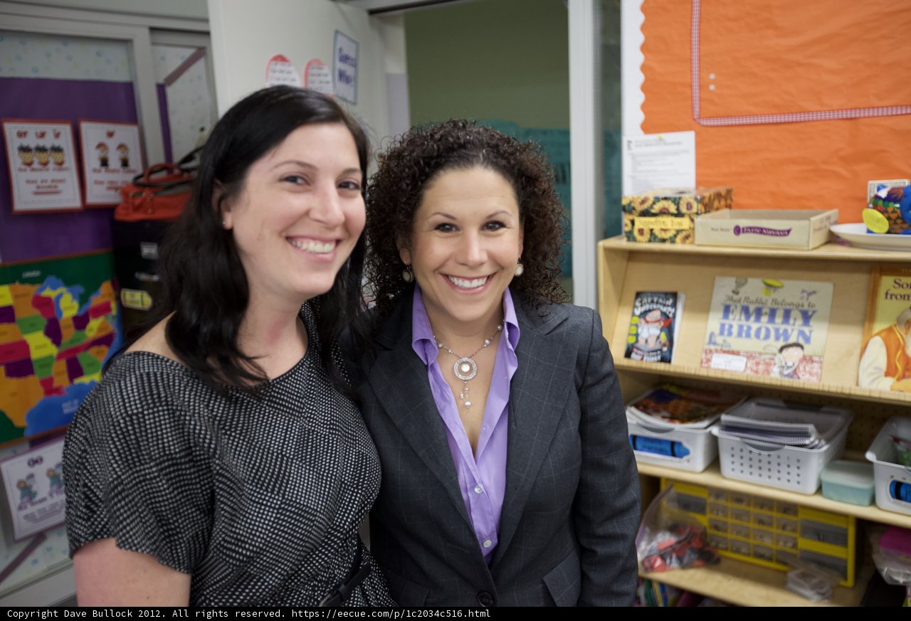 Two Women with Accessories in Front of Classroom Shelf