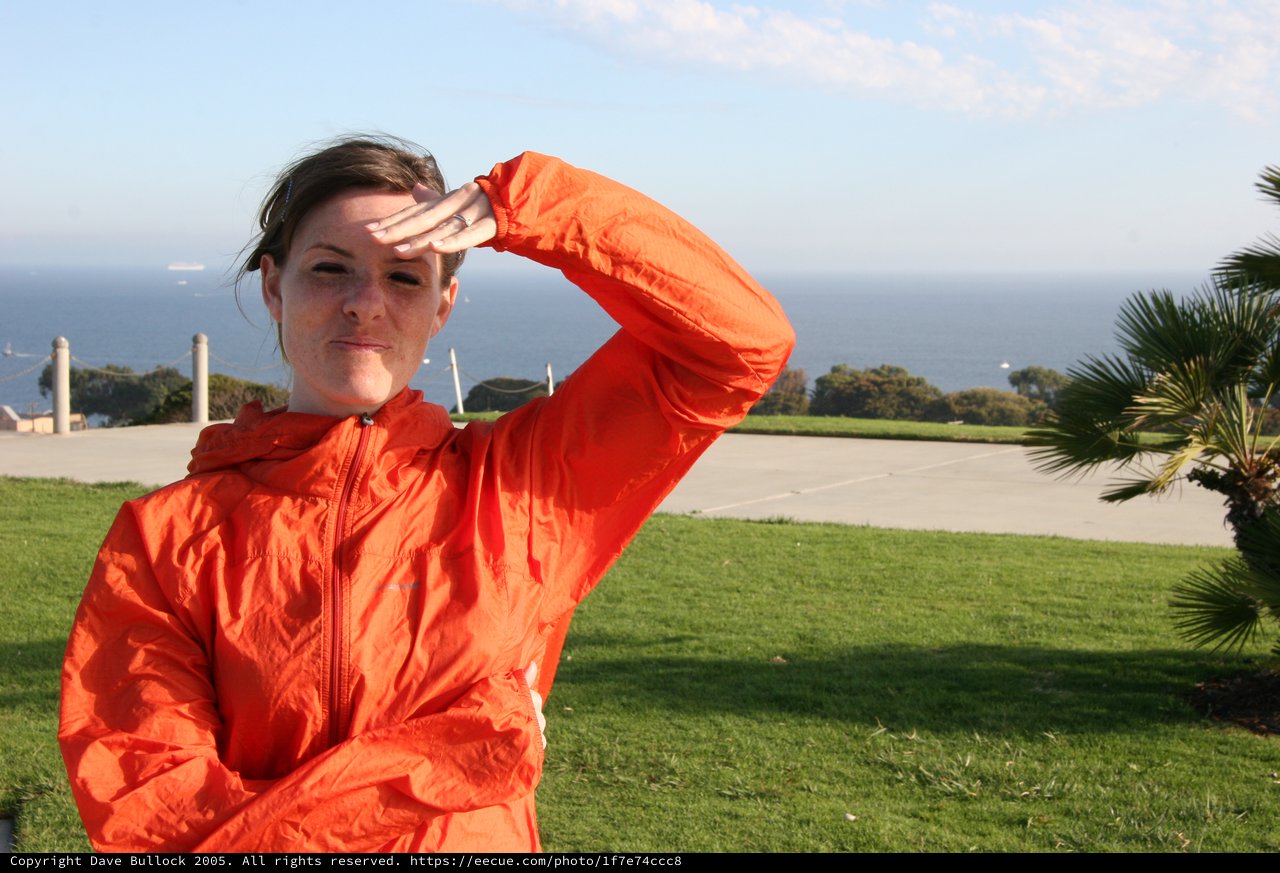Woman in Orange Jacket Shielding Eyes by Ocean