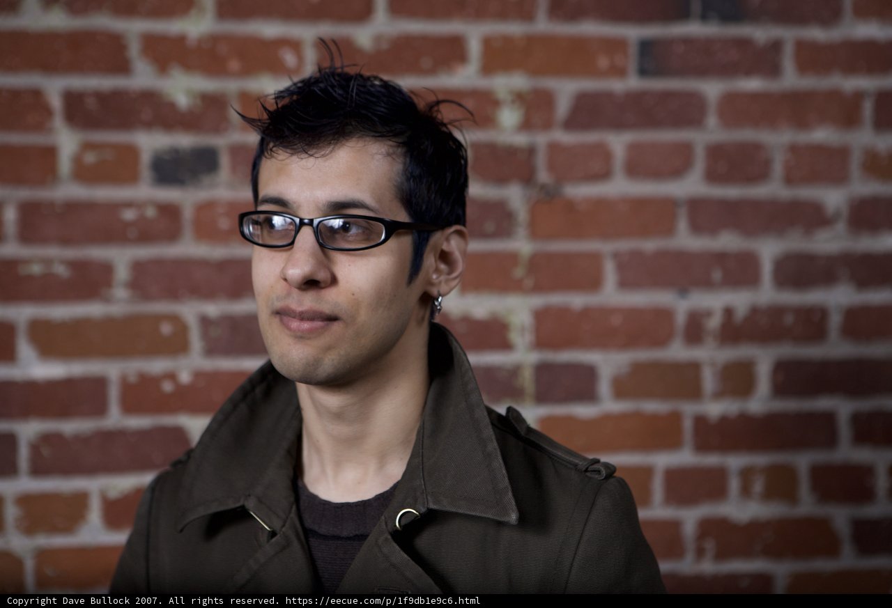 Smiling Man in Jacket and Glasses Poses by Brick Wall