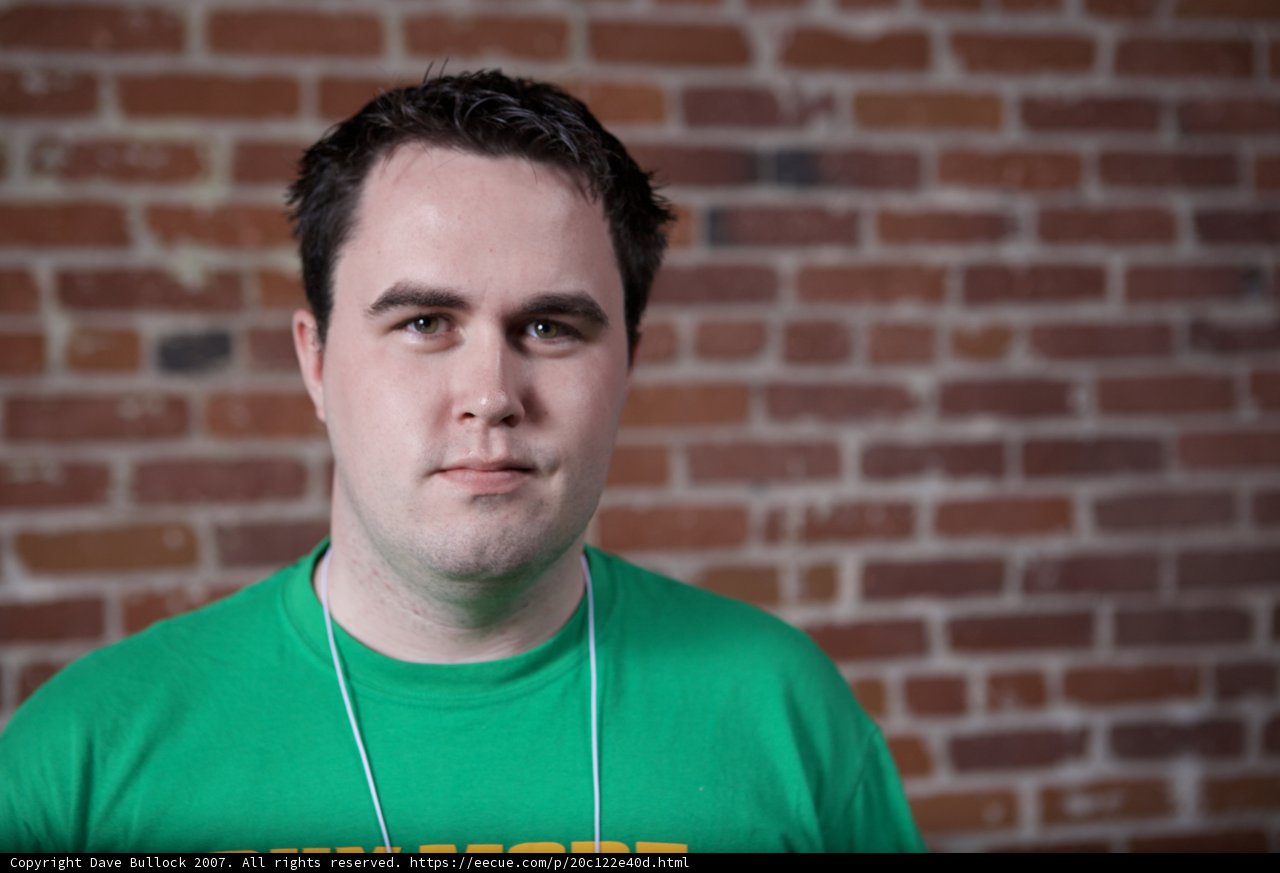 Man in Green T-Shirt Poses Against Brick Wall