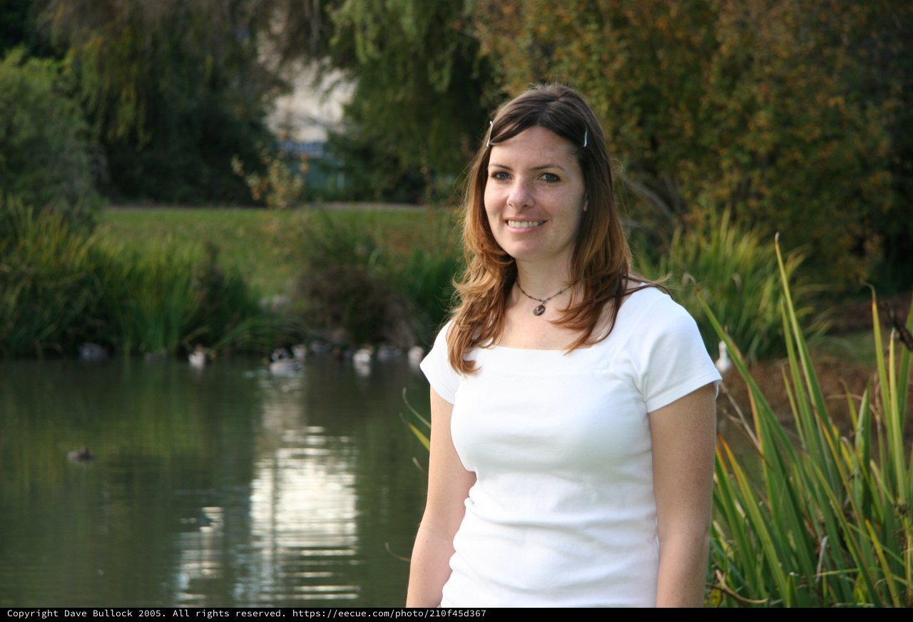 Young Woman Smiling by a Tranquil Park Pond