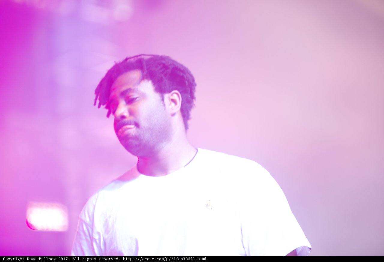 Sampha's Time to Shine        Caption: British singer-songwriter Sampha, wearing a white T-shirt and purple undershirt, takes center stage and beams with happiness while performing at Coachella 2017, with the spotlight illuminating his face and microphone.