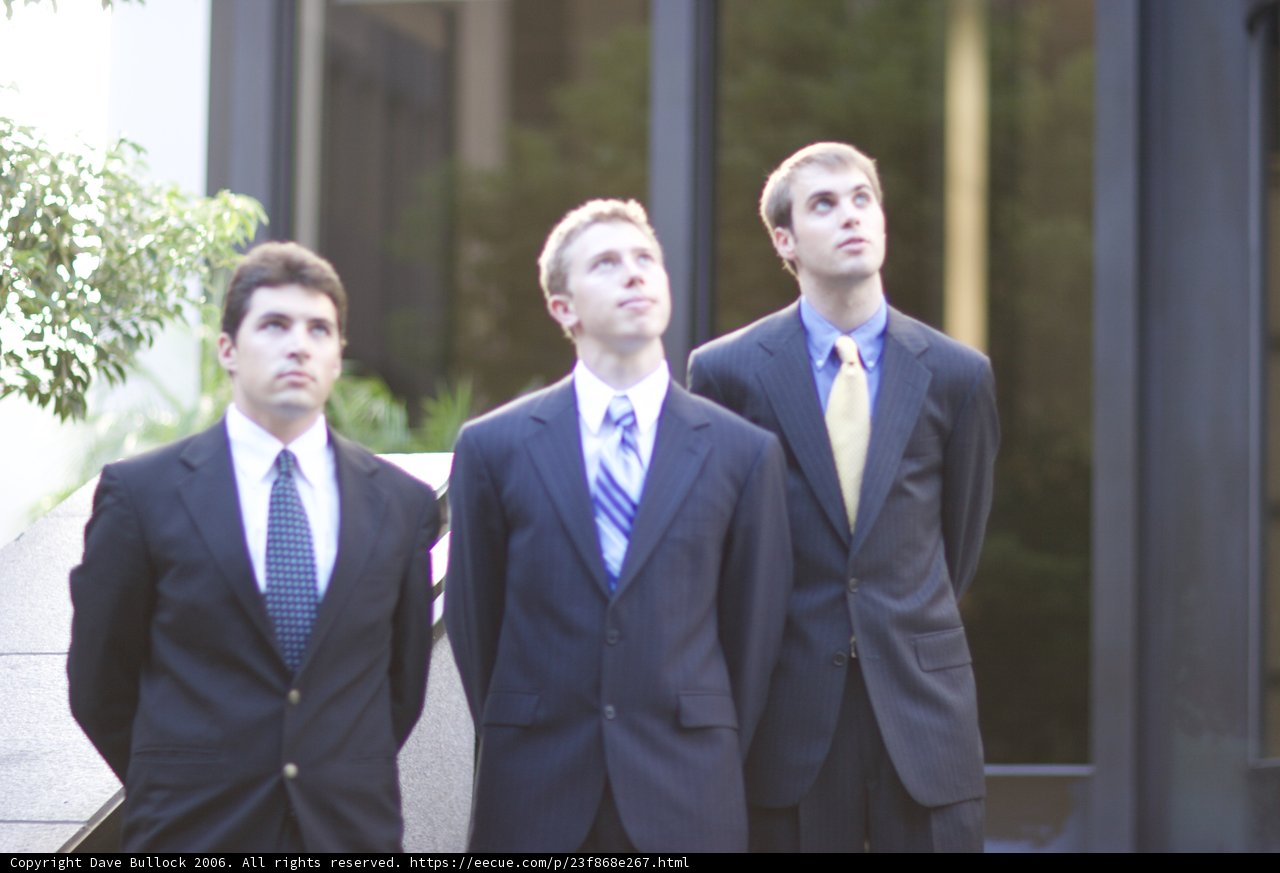 Three Men in Suits Pose in Front of Building