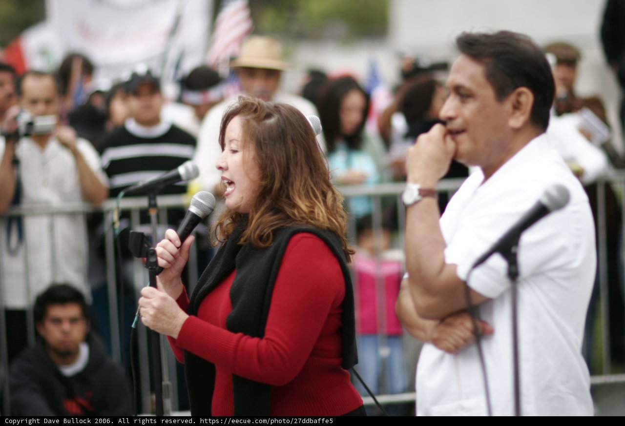 Empowering the Crowd Caption: A woman delivers a passionate speech as she holds up a microphone in front of a diverse and engaged audience at a 2006 student protest.
