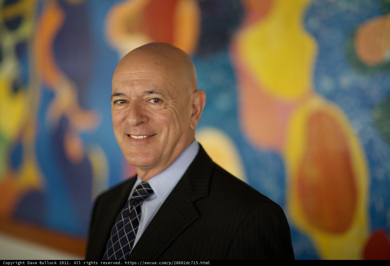 Bald Man in Suit and Tie Stands in Front of Colorful Painting
