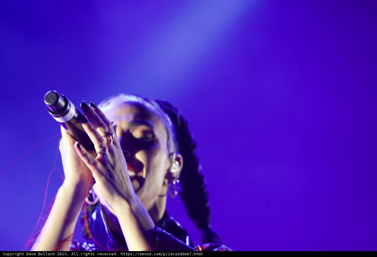 FKA twigs Emotional Portrait Eyes Closed Looking Up Baby Hairs Hoop Earrings Red Lipstick Braided Ponytails Both Hands Holding Microphone Rings Dark Nail Polish Purple Blue Lighting