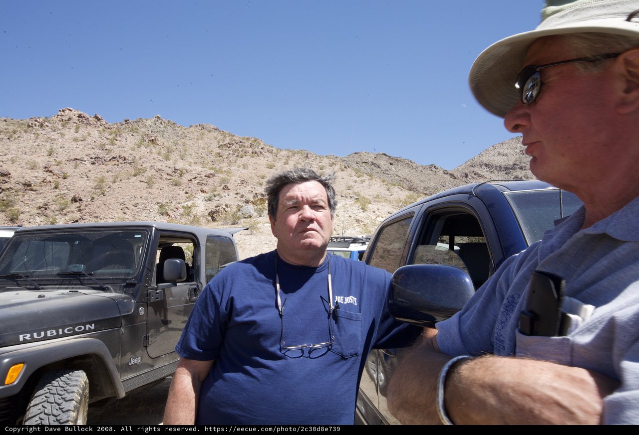 Two Men Conversing Beside Jeeps in Desert Terrain