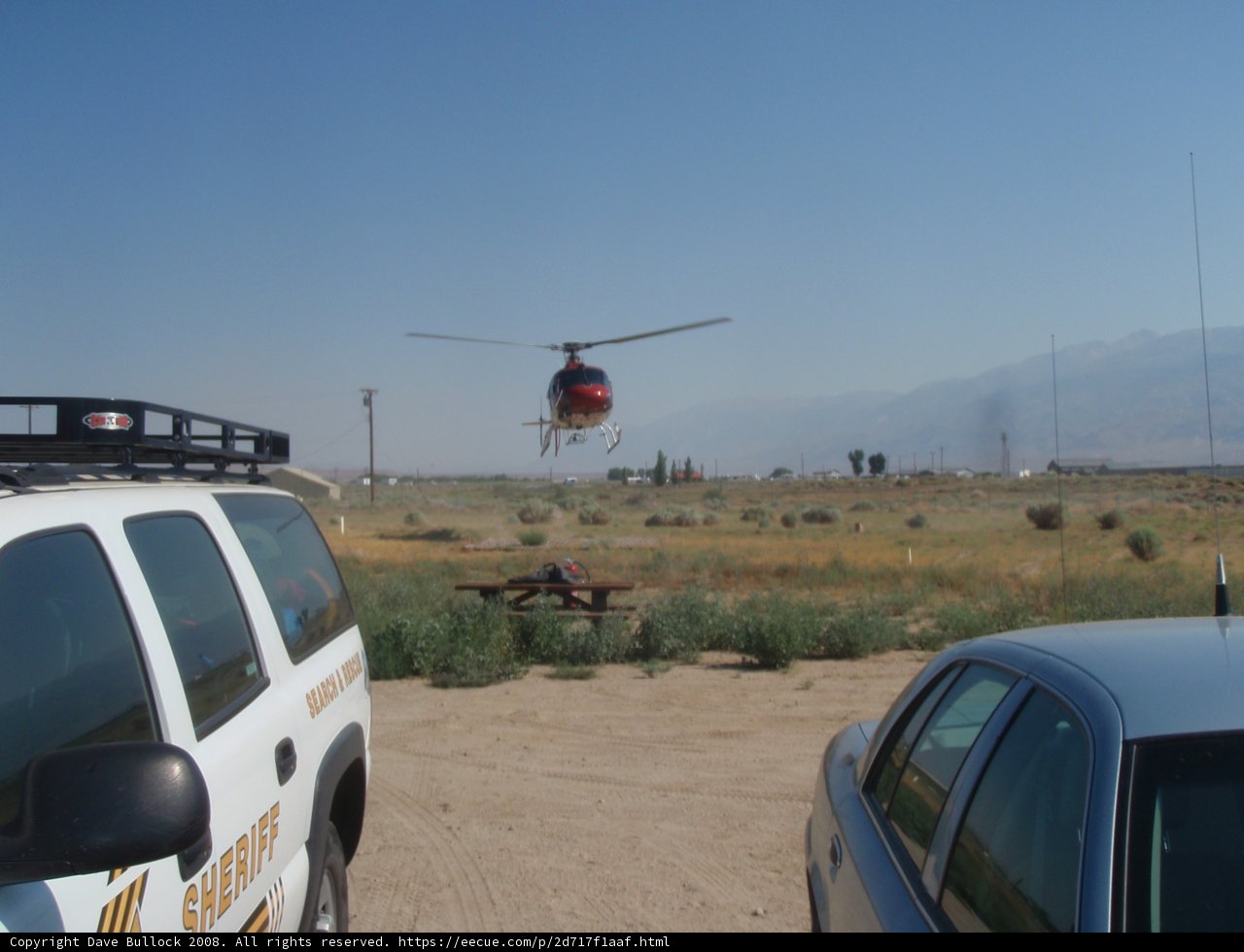 Helicopter in Flight Over a Field with a Car in the Background