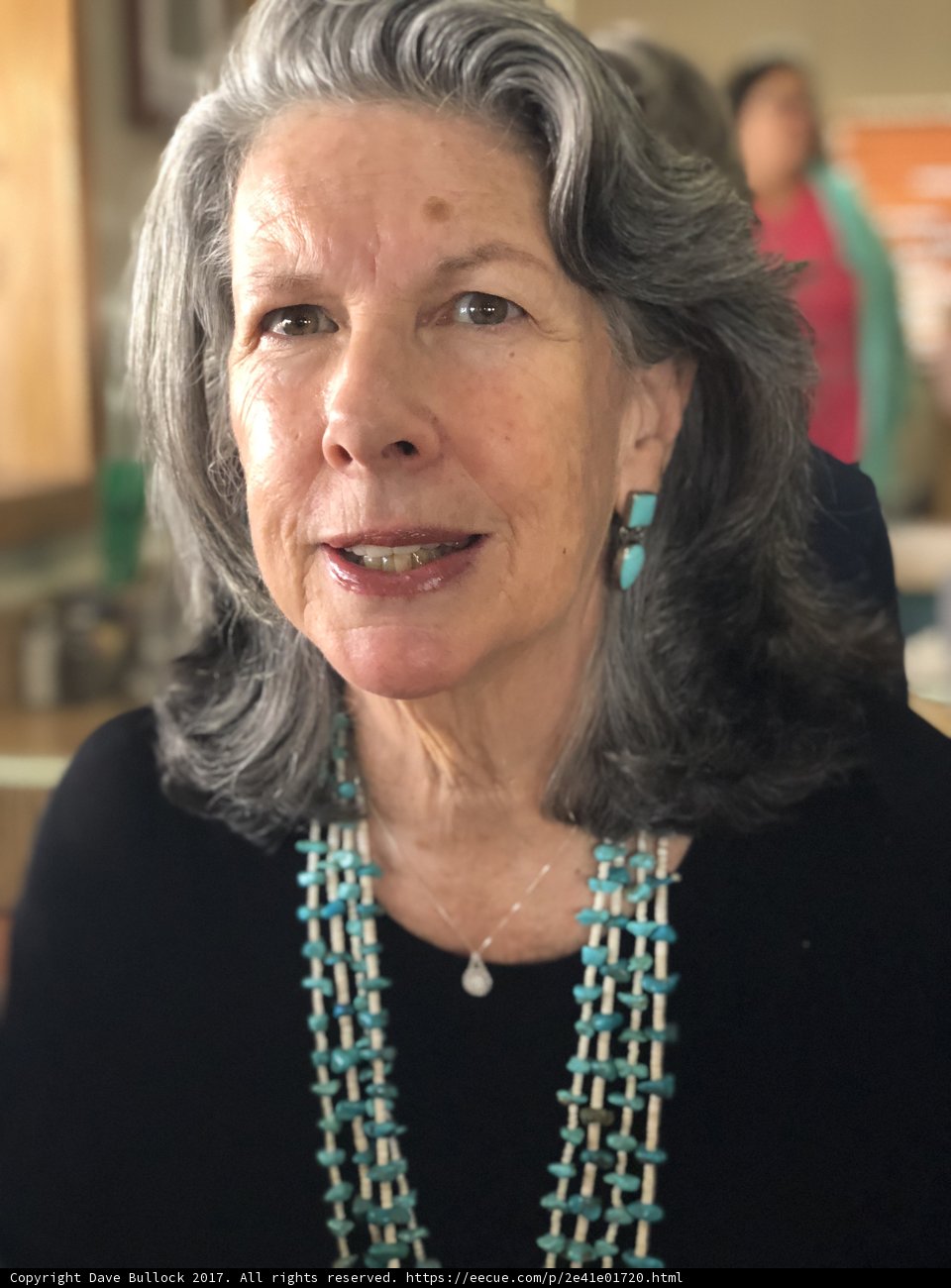 Gray-haired woman wearing a bead necklace and glasses