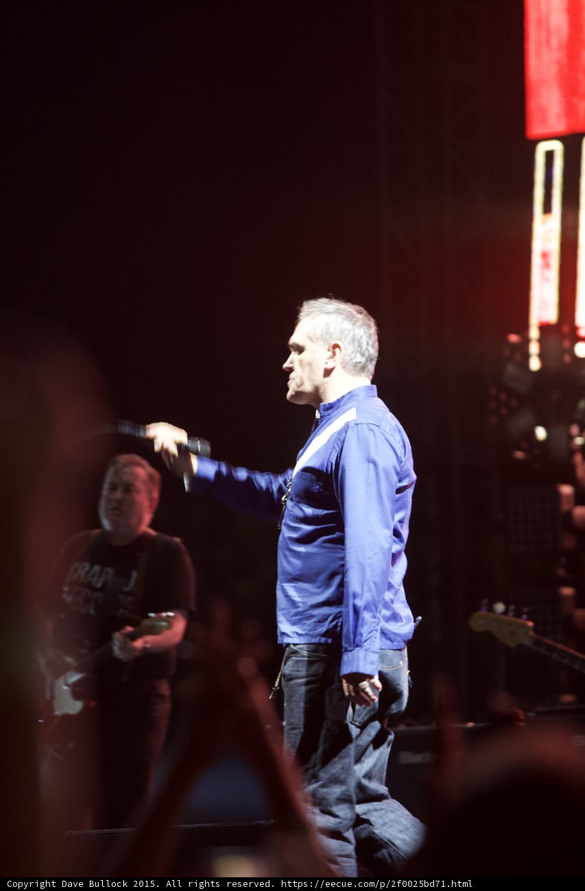 Morrissey Profile Blue Shirt Holding Mic Guitarist Capitol Tee Red Video Screen Dark Stage