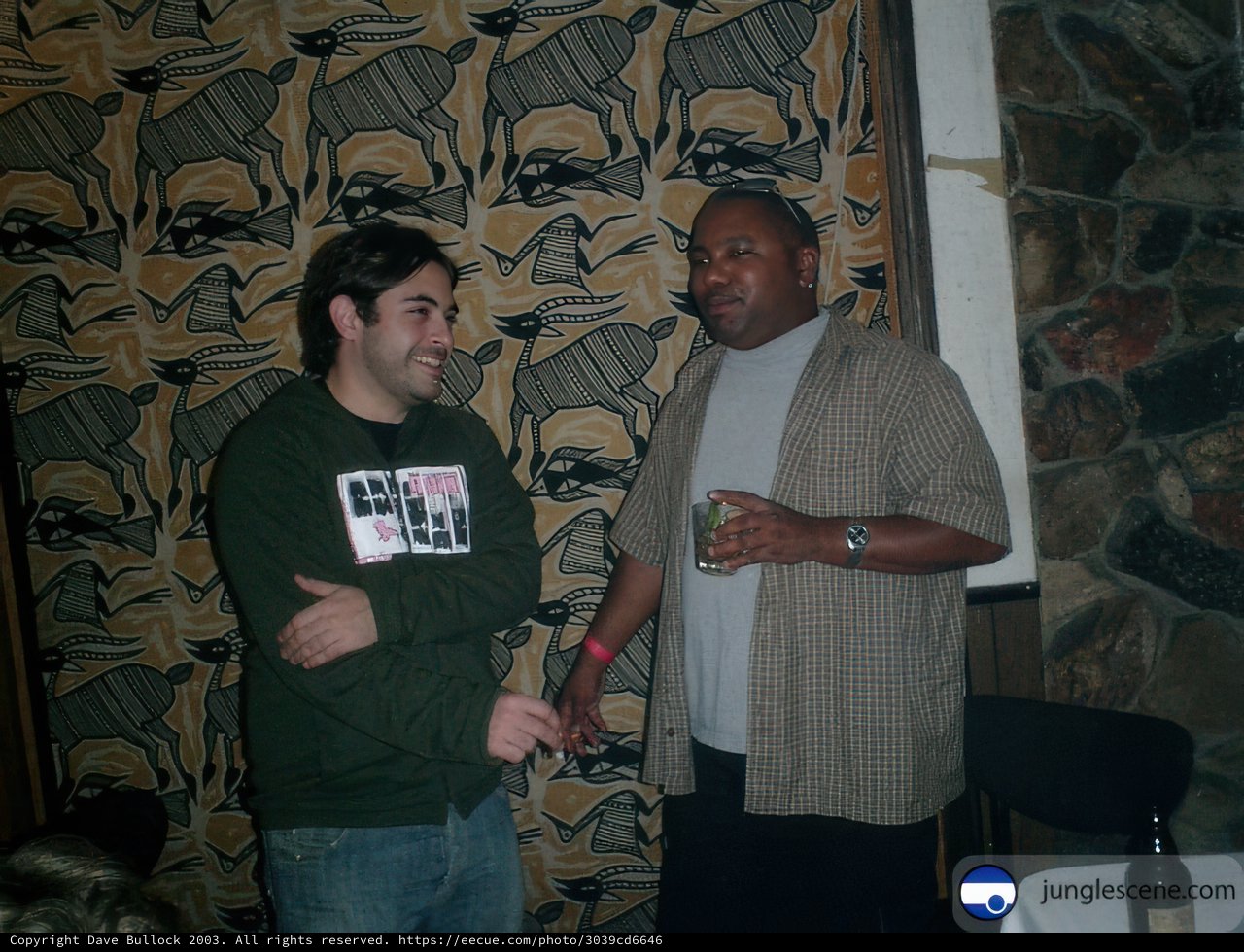 Two Men in Casual Attire Stand Before Wall