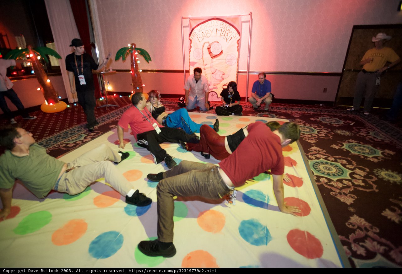 Giant game night with family and friends Caption: A group of people, including children and adults, gather together in a living room to play on a giant game. The flooring and footwear are visible, along with various clothing and accessories.