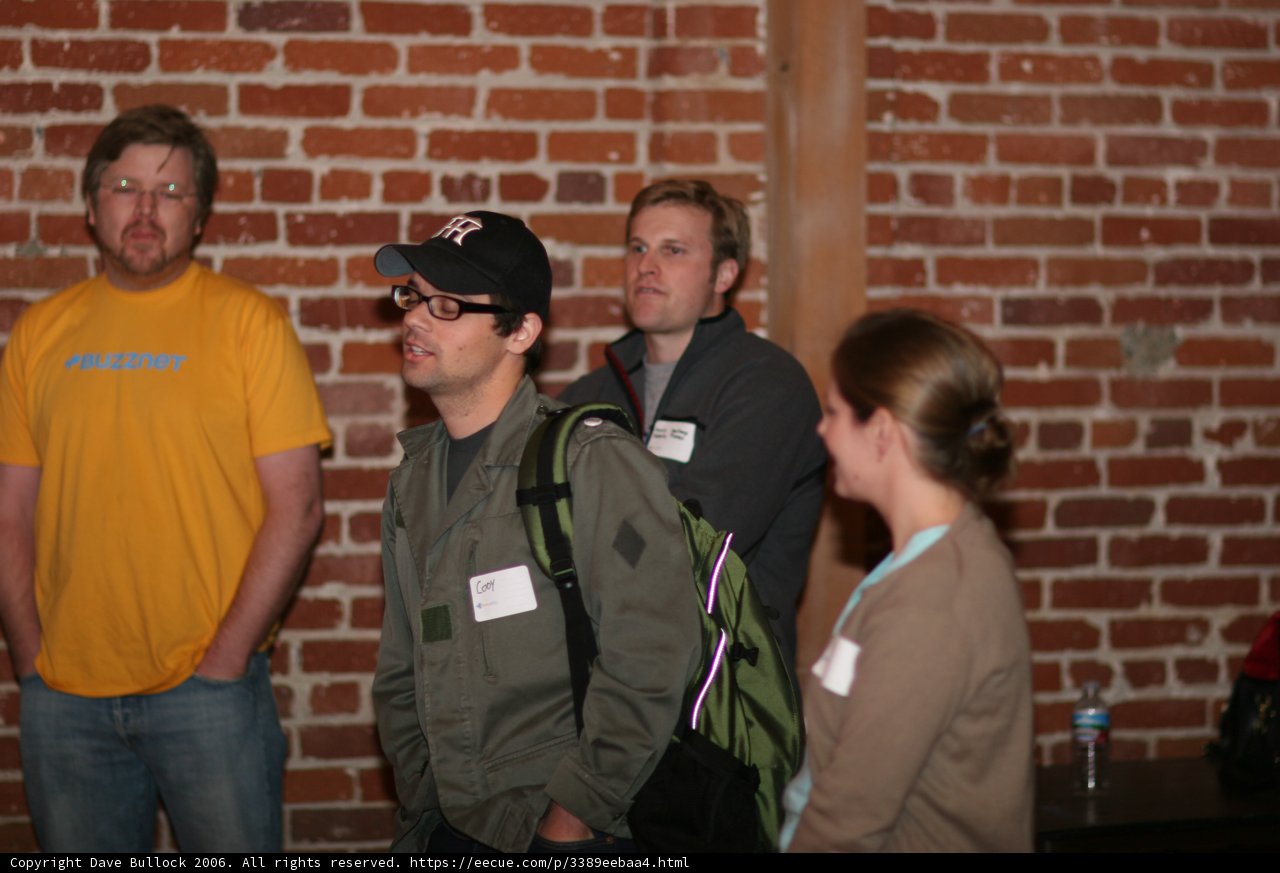 Group of Four People in Baseball Caps Pose in Front of Brick Wall
