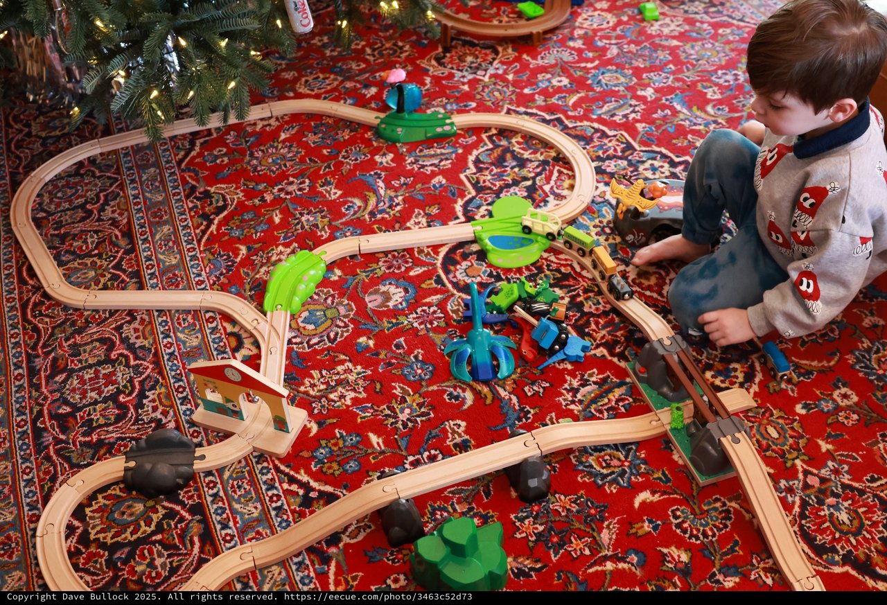 Child Playing with Wooden Train Set Under Christmas Tree